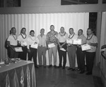 Nine men stand in a line. Most are wearing leis and all but one are holding a certificate by Squire Haskins Photography Inc.