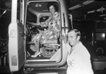 Woman, smiling and wearing a flower-printed dress sits in the driver's seat of a semi tractor. A man , also smiling, stands on the ground, wearing a sport coat and tie. by Squire Haskins Photography Inc.