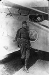 Photograph of a man in military uniform standing beside a bi-plane. Sitting the in cockpit is a woman wearing a hat. by Squire Haskins Photography Inc.