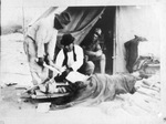 A Mexican soldier lying on ground outside tent with medic applying cast to his leg
