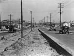 Cars and a tractor driving on a divided, newly made street