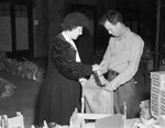 William L. Howard holds bag open while Mrs. W.H. French, representing Catholic Daughters, deposits gifts into the Goodfellows' Christmas bags at the Pioneer Palace, 12/21/1937