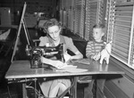 Liberator Village. Mrs. C. H. Ragsdale using sewing machine as her son, Howard, stands by.