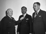 Colonel Herbert Baldwin pins merit ribbons on B. Kirk, right, and M. Vargas Junior, civilian employees of the Army Finance Department