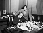 Amon Carter Junior and unidentified man singing paper's in Mr. North's office