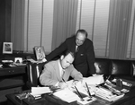 Amon Carter Junior and unidentified man signing paper's in Mr. North's office