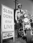 J. L. Cashion, traffic officer, on motorcycle by safety sign