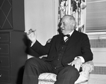 Senator Connally seated in chair, holding cigar next to cabinet