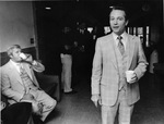 T. Cullen Davis stands in hallway during trial proceedings, ca. 02/1977; Phil Burleson, attorney, sits on bench at left