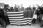 Crowd of protesters holding United States flag at Ku Klux Klan march in downtown Dallas by Rodger Mallison