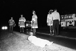 Automobile crash involving a Corvette in which one person was killed; body on side of road surrounded by EMT fireman, 11/30/1980 by Gene Gordon
