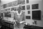 Texas Christian University (T. C. U.) English professor Betsy Colquitt standing in front of artwork and holding a book at her home near Texas Christian University (T. C. U.)