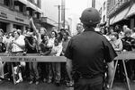 Dallas police officer looking at a crowd of protesters at Ku Klux Klan march in downtown Dallas by Joe Giron