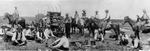 Cowboys around a chuck wagon, some on horseback and others sitting on the ground