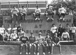 Fraternity men wearing t-shirts with Greek letters sitting in front of UTA sign