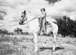 A woman in cowgirl attire sits on a horse by W. D. Smith