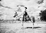 A woman in cowgirl attire sits on a horse by W. D. Smith