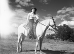 A woman in cowgirl attire sits on a horse by W. D. Smith