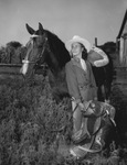 Mitzi Lucas holding a saddle and standing next to a horse by W. D. Smith