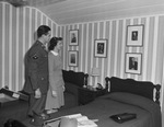 A young man in a military uniform and a young woman look at portraits on a bedroom wall by W. D. Smith