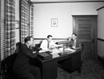 Men sitting at a desk in an office by W. D. Smith