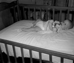 A baby girl lying in her crib and holding a toy by W. D. Smith