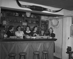 Six women holding glasses while standing behind a bar by W. D. Smith