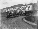 Two men sitting on horse-drawn wagon in front of Armour & Company building, Fort Worth Stockyards