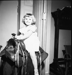 A young girl in a dress sitting on a saddle display by W. D. Smith