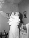 A woman holding a baby next to a crib by W. D. Smith